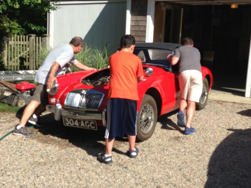 fathers and sons working on red classic car MGA